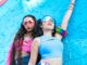 Two females in crop tops leaning on a blue wall